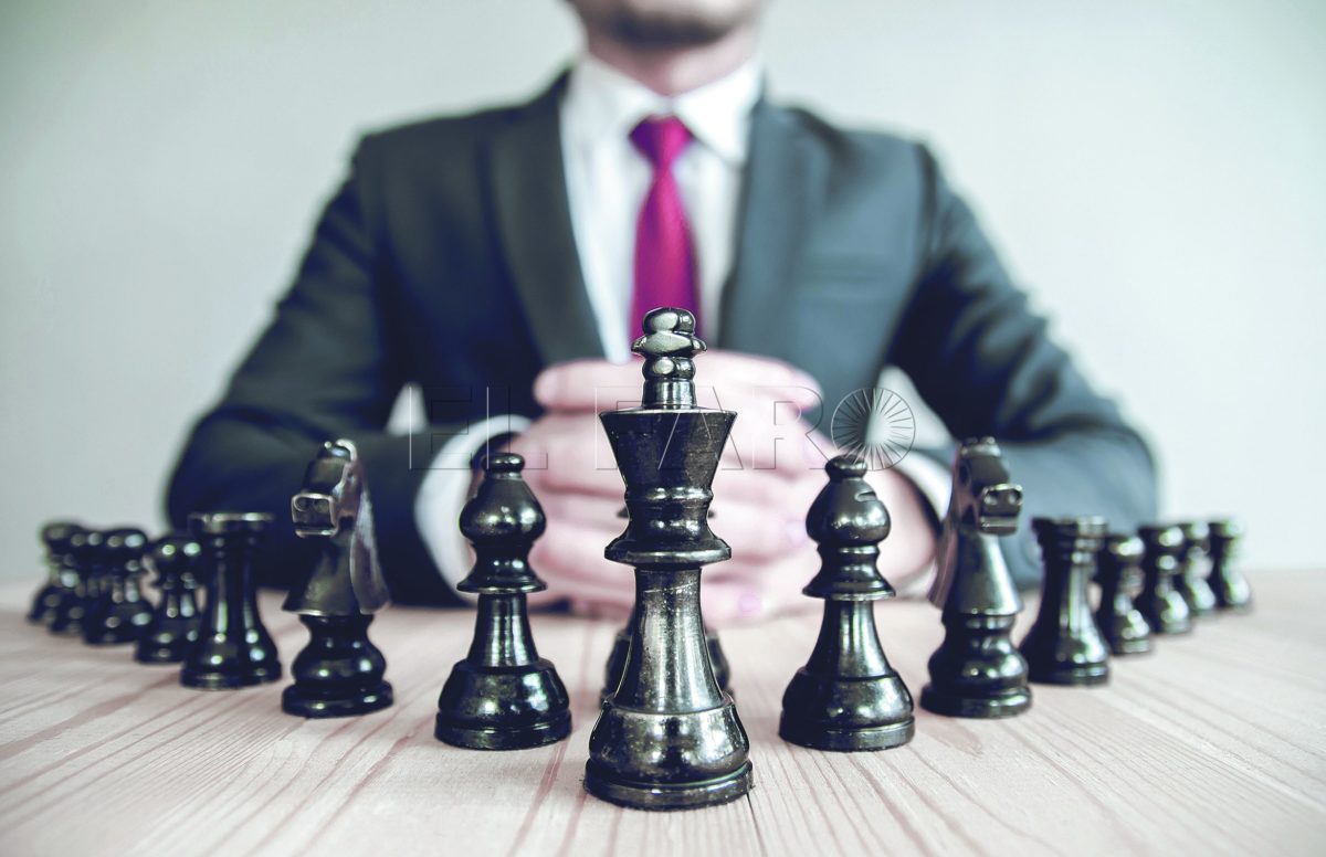 Retro style image of a businessman with clasped hands planning strategy with chess figures on an old wooden table.