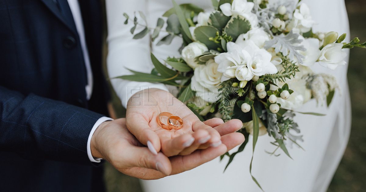 Wedding bands in the hands of bride and groom and with beautiful wedding bouquet made of greenery and white flowers