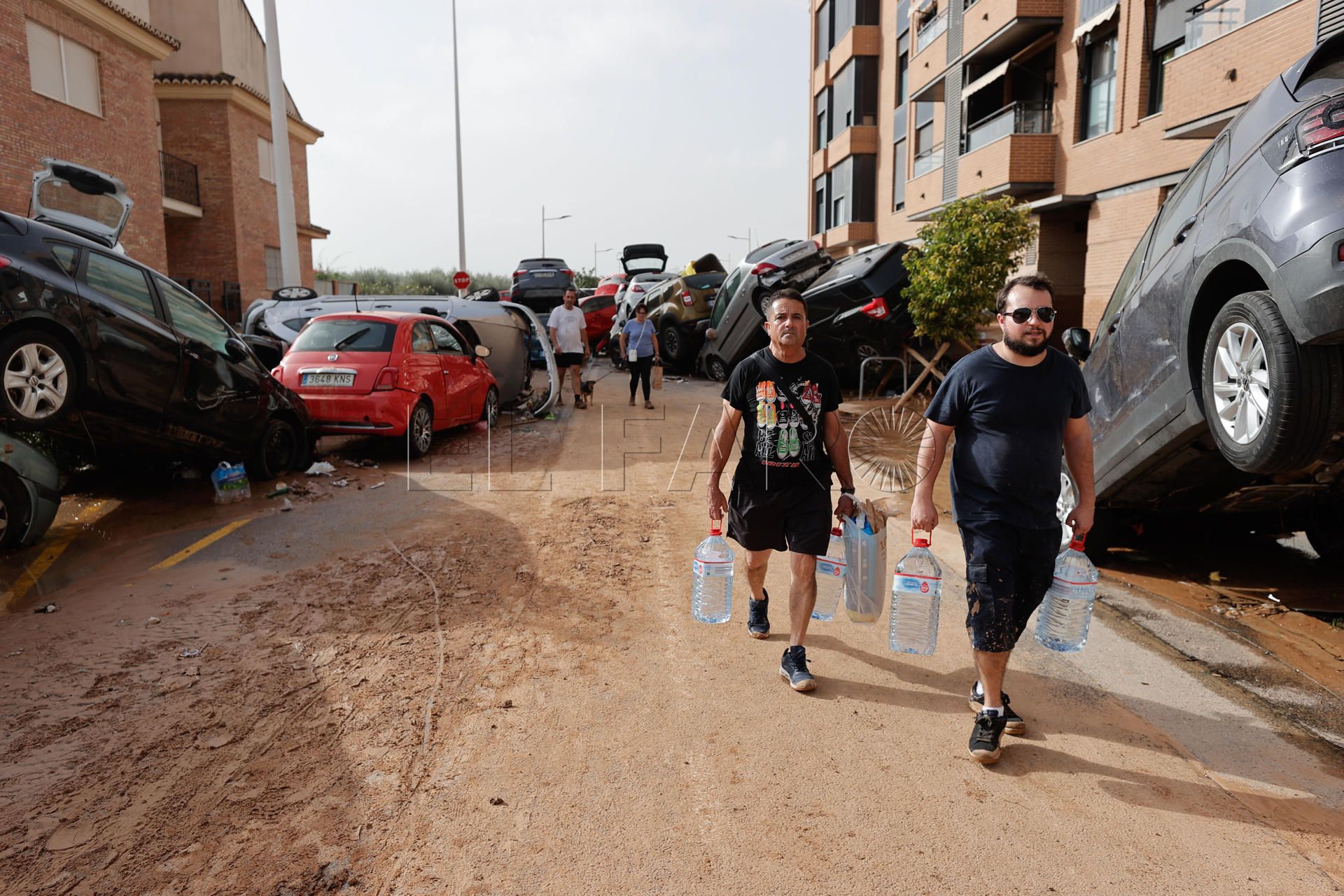PAIPORTA (VALENCIA), 30/10/2024.- Varias personas con botellas de agua caminan entre los vehículos destrozados en la región valenciana de Paiporta a causa de las fuertes lluvias causadas por la DANA. La alcaldesa de Paiporta (Valencia), Maribel Albalat, ha confirmado que al menos hay 34 fallecidos en su municipio a consecuencia de la dana que ha afectado a la Comunidad Valenciana.  EFE/Manu Bruque